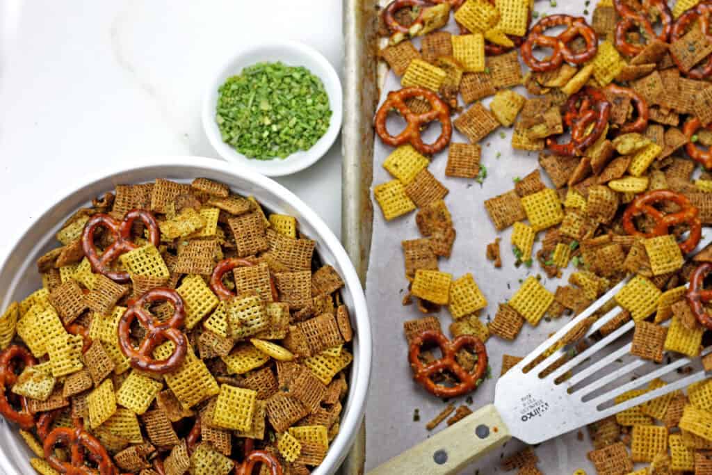 Ranch chex mix in a bowl next to a sheet pan of ranch chex mix