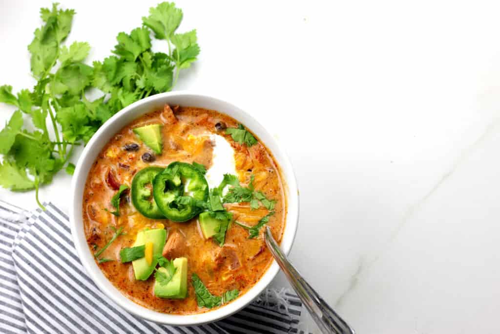 Close up of creamy enchilada soup with a spoon in the bowl on a white countertop