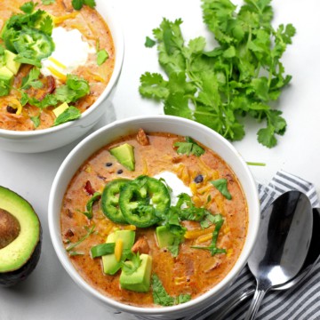 Overview of two bowls of creamy enchilada soup with a spoon in the bowl on a white countertop