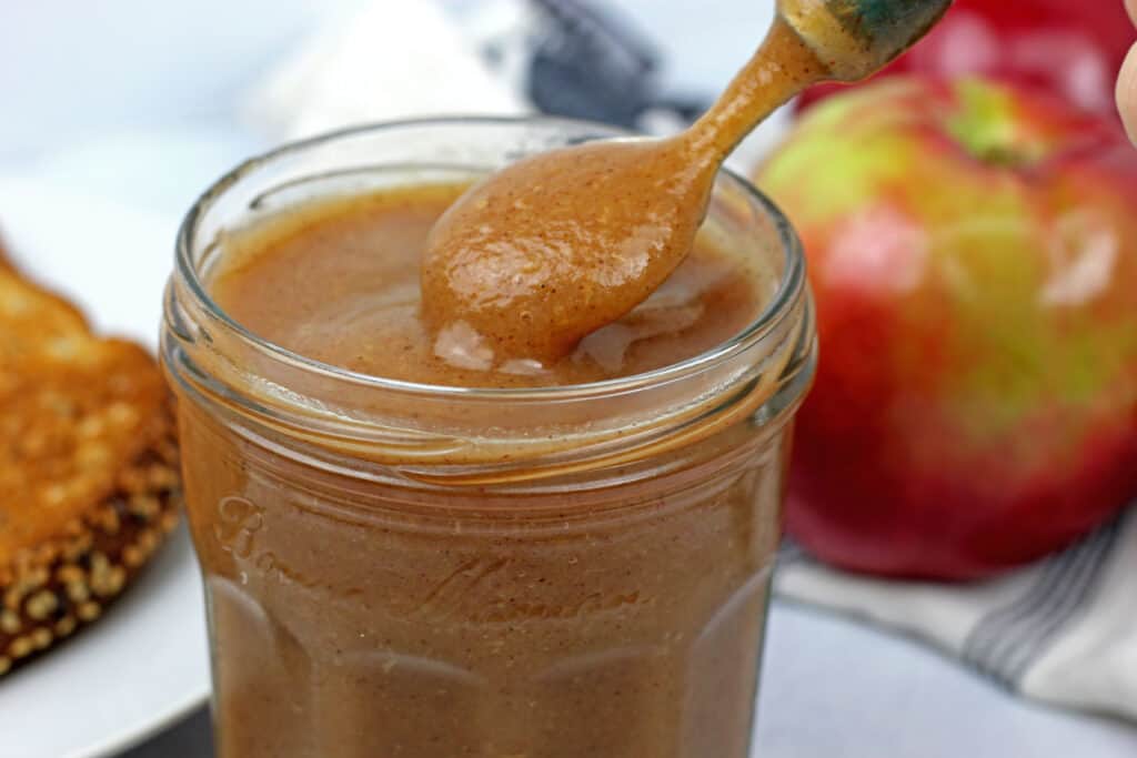 Apple butter on a spoon above a jar of the instant pot apple butter