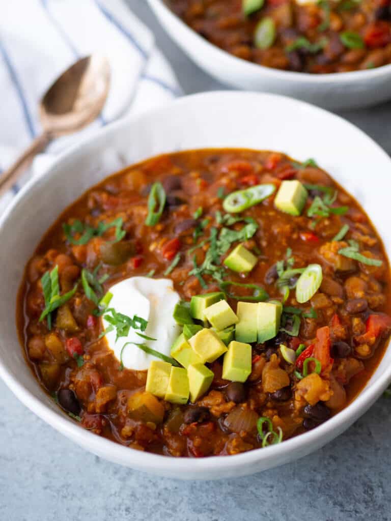 Ground turkey slow cooker recipe with chipotle pumpkin turkey chili on a gray background with a white napkin and gold spoon