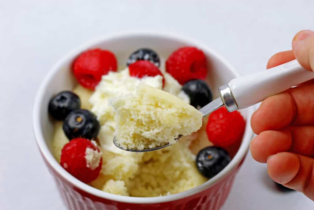 Close up of a bite of the vanilla mug cake with the cake in the background on a white surface.