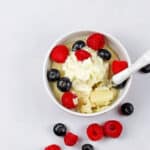 Overview of the vanilla mug cake with a white spoon on a white surface with whipped cream and mixed berries.