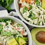 overview of two buffalo chicken rice bowl with an avocado, cilantro, forks, and a napkin on the side on a white background. Also has the words "buffalo chicken rice bowls" on the photo.