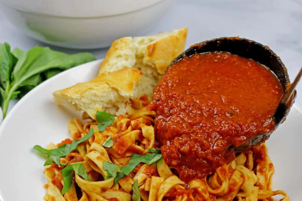 a bowl of pasta and bread with a ladle of instant pot marinara sauce going on top.