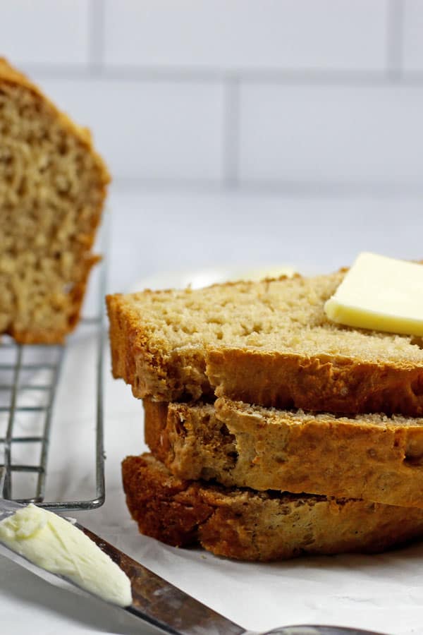 3 slices of 3 ingredient beer bread stacked with pat of butter on top on a white background with the loaf of beer bread in the background and a butter knife in the foreground