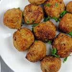White plate of air fryer turkey meatballs on a white background with a blue and white napkin and a white bowl of tomato sauce on the side on the side.