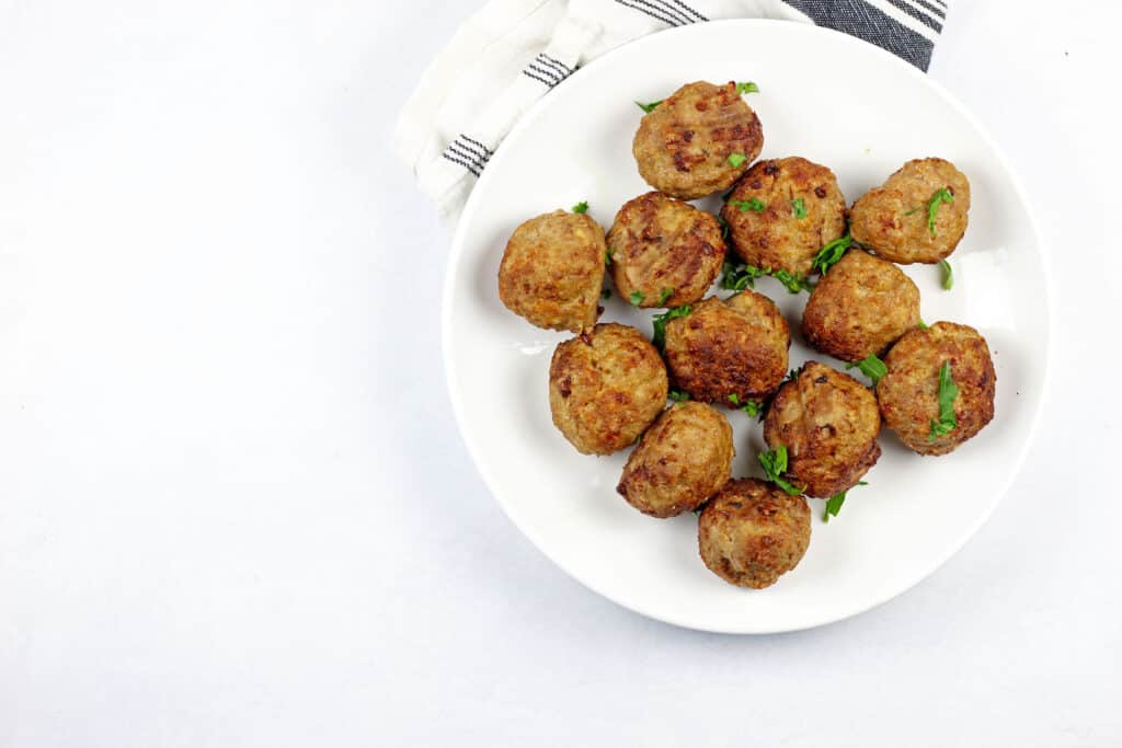 White plate of air fryer turkey meatballs on a white background with a blue and white napkin on the side.