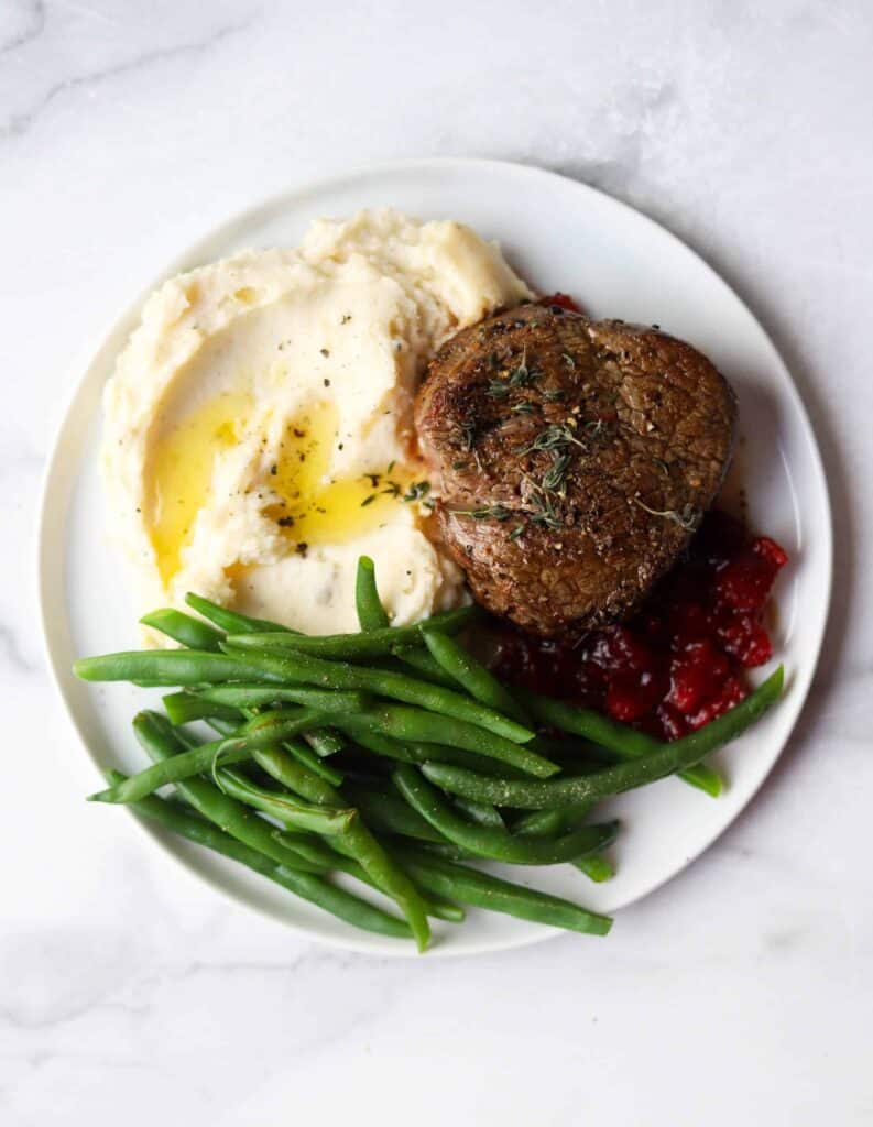 One of the best valentine's day recipes with a white plate of beef, cranberries, green beans, and mashed potatoes.
