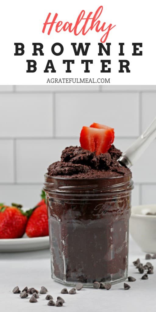 Pinterest image of a jar of edible brownie batter with chocolate chips and strawberries on the side and a white spoon in the batter. It's on a white subway tile background.