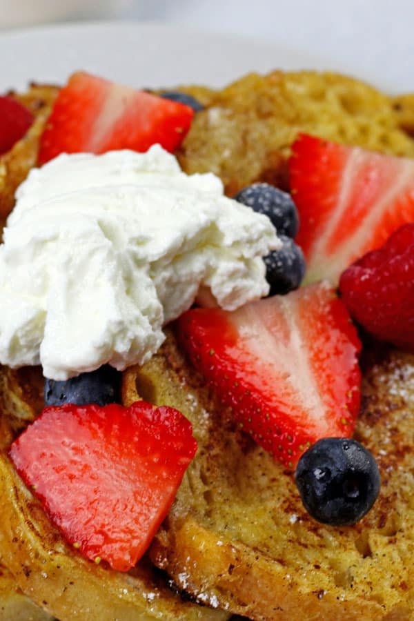 Close up of sourdough french toast with strawberries, blueberries, and yogurt on top on a white plate.