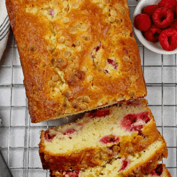The White Chocolate and Raspberry Loaf Cake on a cooling rack sliced with a small bowl of raspberries on the side.