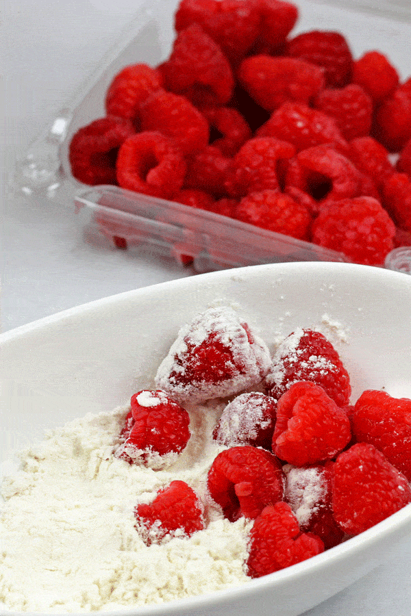 A container of raspberries with a bowl of flour used to toss the berries in.