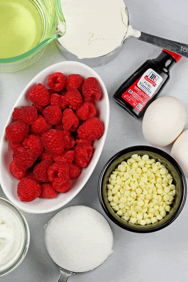 Ingredients for White Chocolate Loaf Cake laid out on a white background including vanilla extract, eggs, sugar, flour, greek yogurt, white chocolate chips, and vegetable oil.