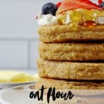 A stack of gluten free oat flour pancakes with syrup dipping down the sides topped with yogurt and berries with white subway tile in the background. The text overlay says "oat flour pancakes."