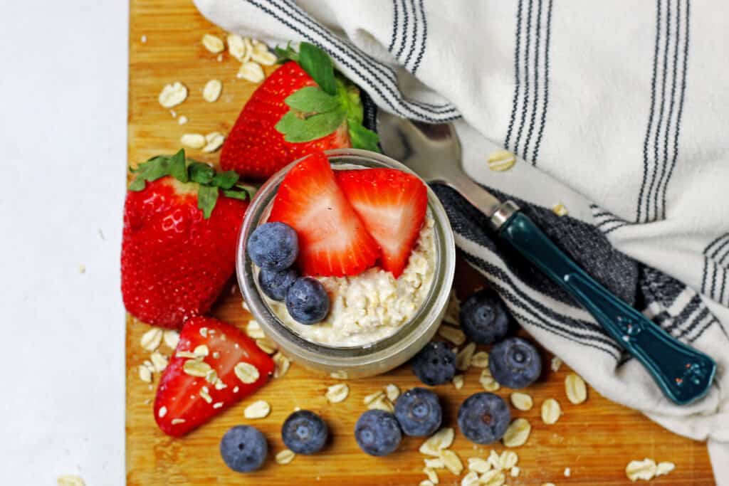 An overview of the top of the vanilla overnight oats with berries on top and a napkin and spoon on the side and oats scattered around.