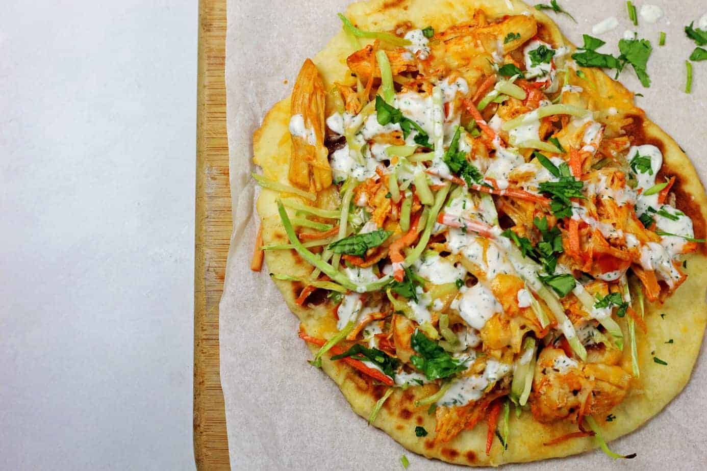 A buffalo chicken flatbread sitting on top of a parchment paper lined cutting board on a white counter.