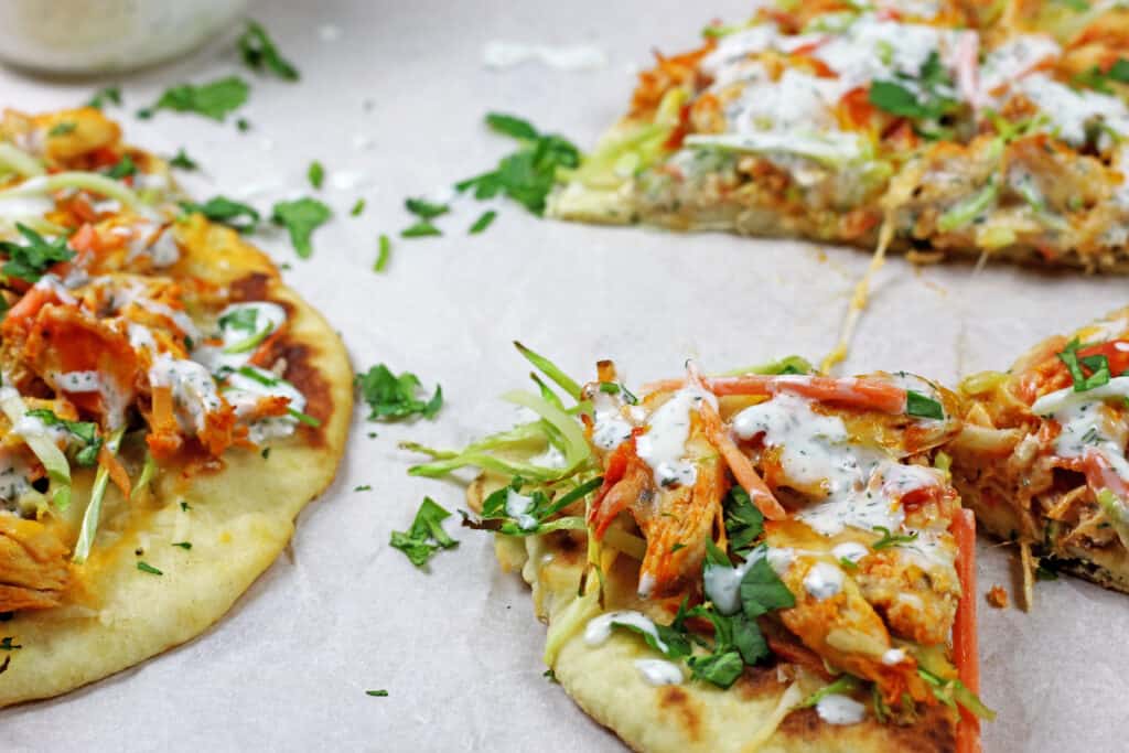 Slices of buffalo chicken flatbread with cilantro scattered around the parchment paper.