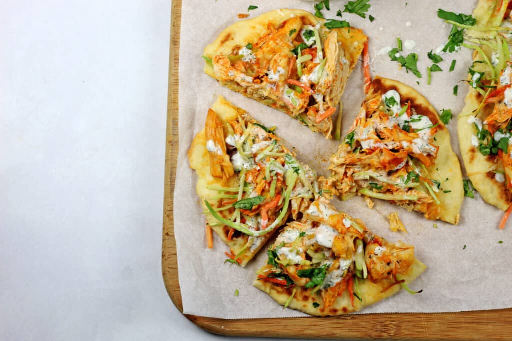 A buffalo chicken flatbread that is sliced in four pieces on a parchment paper lined cutting board on a white countertop.