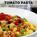 Picture of the tiktok feta pasta with cherry tomatoes in a white bowl with lemon, basil, and wine glasses in the background. One of the wine glasses has a red wine in it. The text overlay says "baked feta tomato pasta" and "simple dinner idea" in red and black lettering.