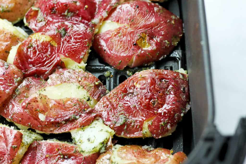 Air fryer smashed potatoes in a black air fryer basket prior to cooking.