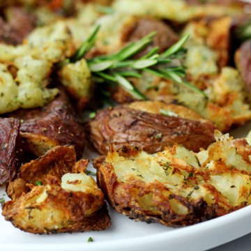 Close up of air fryer smashed potatoes on a white plate garnished with rosemary.