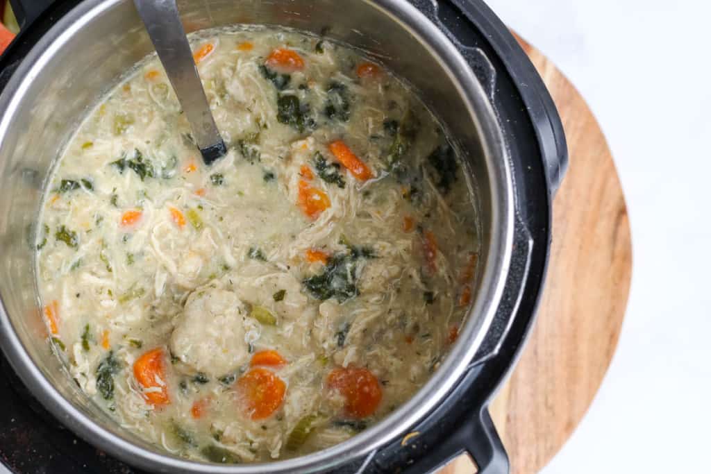 Instant pot with chicken and dumplings in the pot with a stainless steel ladle on a wooden table top.