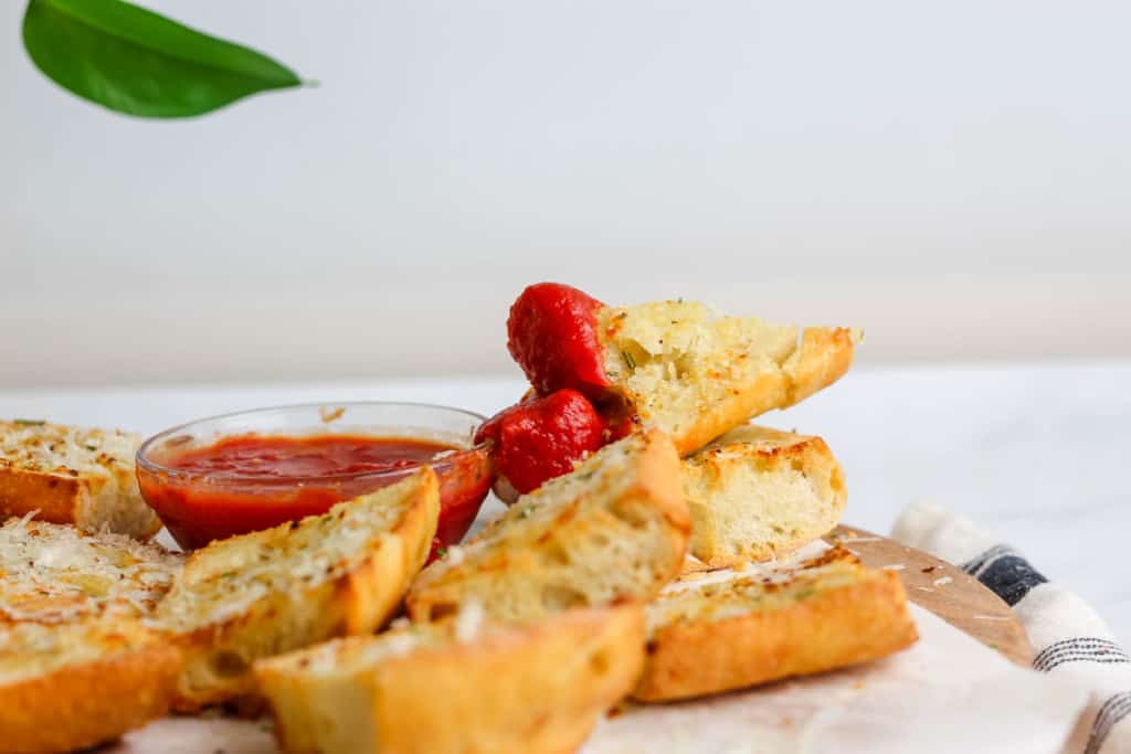 Garlic bread stack on top of each other with one dipped in marinara sauce.