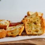 Side view of air fryer garlic bread scattered on white parchment on a wood cutting board.