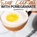Pinterest image of pomegranate whiskey sour on a white surface. The text reads "Whiskey Sour Cocktail with Pomegranate agratefulemeal.com" in a black and brown lettering.