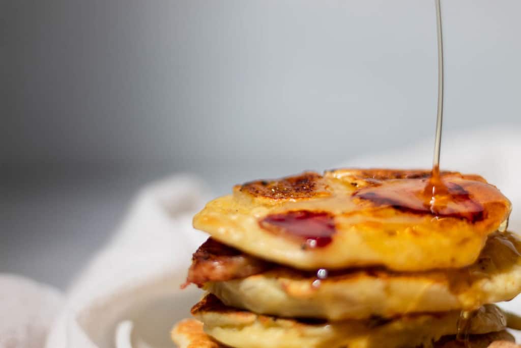 Stack of strawberry banana pancakes with syrup being poured on top.