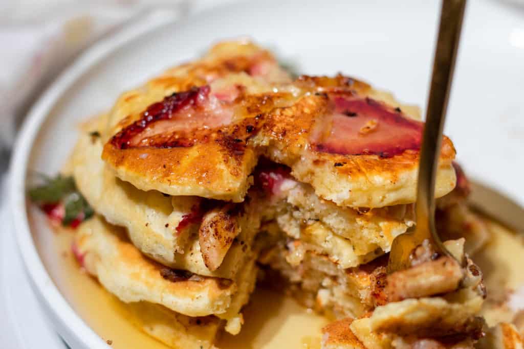 A fork stabbed into a chunk of pancake cut out from a stack of the strawberry banana pancakes.