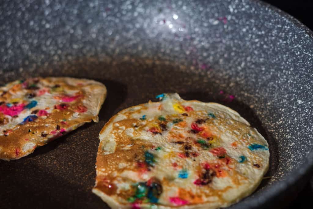 Two confetti pancakes sitting in a non-stick pan.