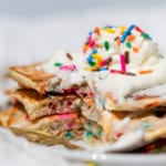 A stack of confetti pancakes with a large bite taken from the side on a white plate and white towel.