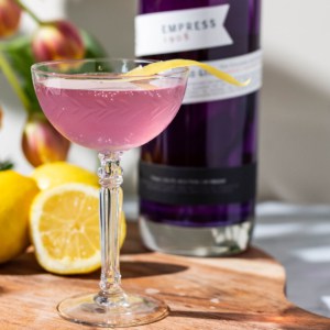 A coupe glass of Empress Gin French 75 on a cutting board with lemons, a bottle of gin, and tulips in the background.