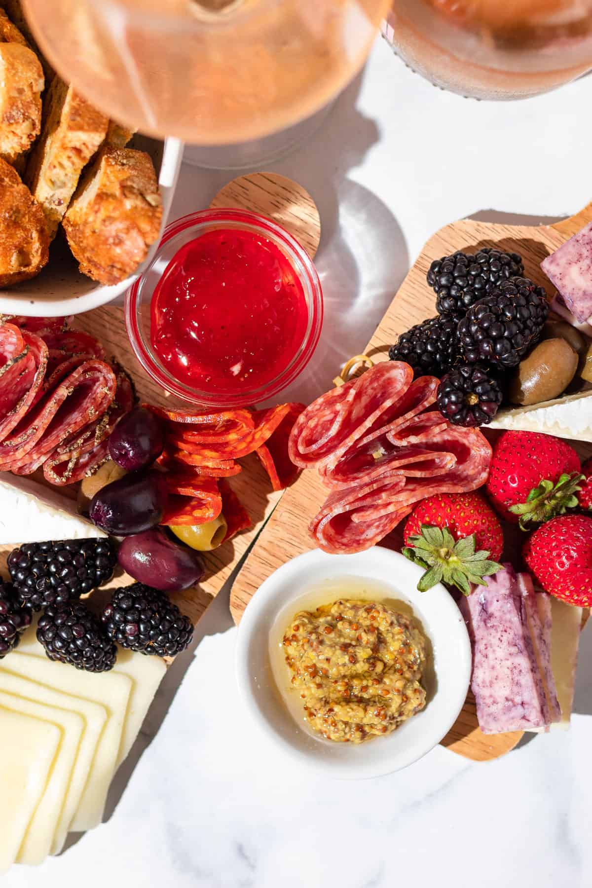 Overview of two charcuterie boards including fruit, meats, cheeses, and sauces and a bowl of bread.