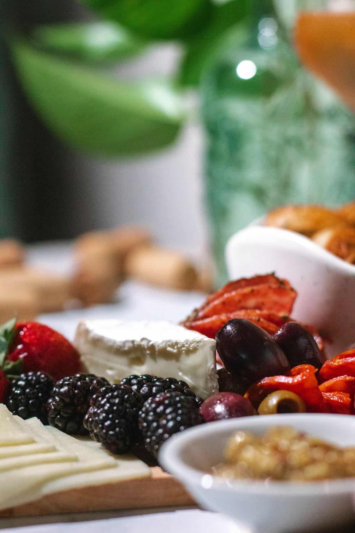 Close view of brie and berries with a bread bowl and green plant in the background.