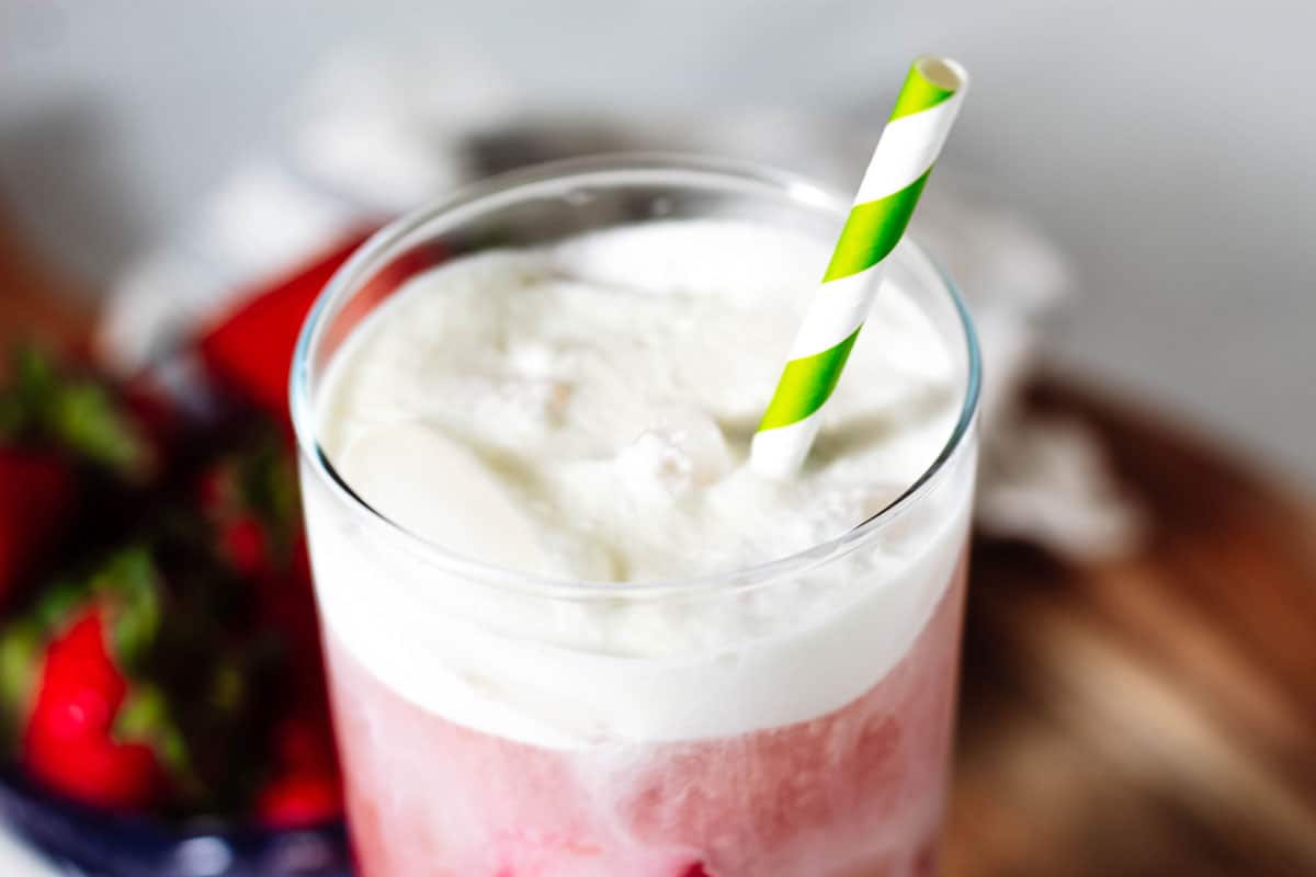 Close up of the top of the pink drink with a green and white paper straw stuck in the cold foam.