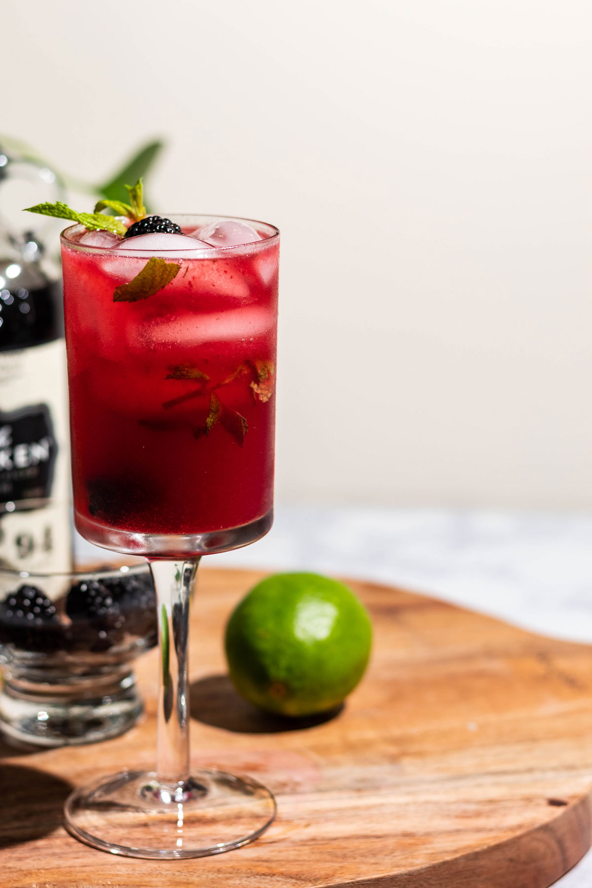 Blackberry mojito on a wood cutting board with a lime and bottle of dark rum behind the glass.