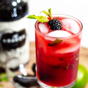 Close up of the blackberry mojito with dark rum in the background and garnished with mint leaves and blackberries.