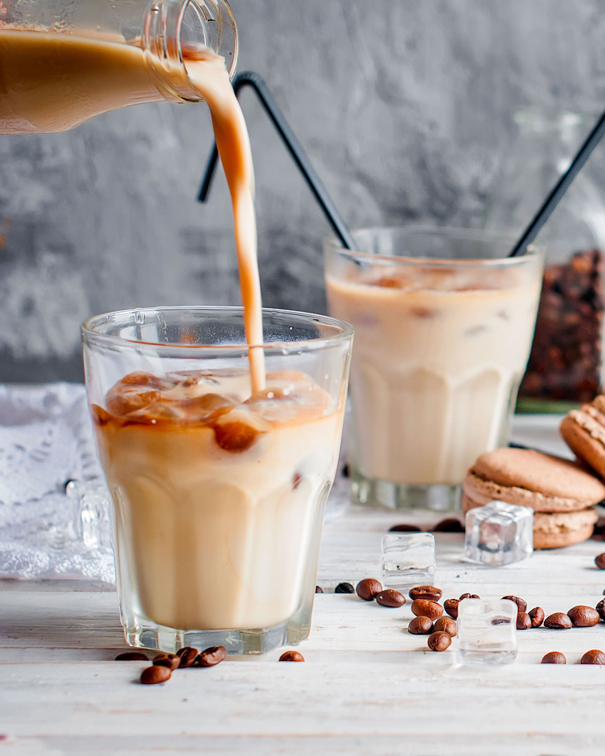 Two iced coffees on a white surface with macaroons and chocolate scattered on the table.