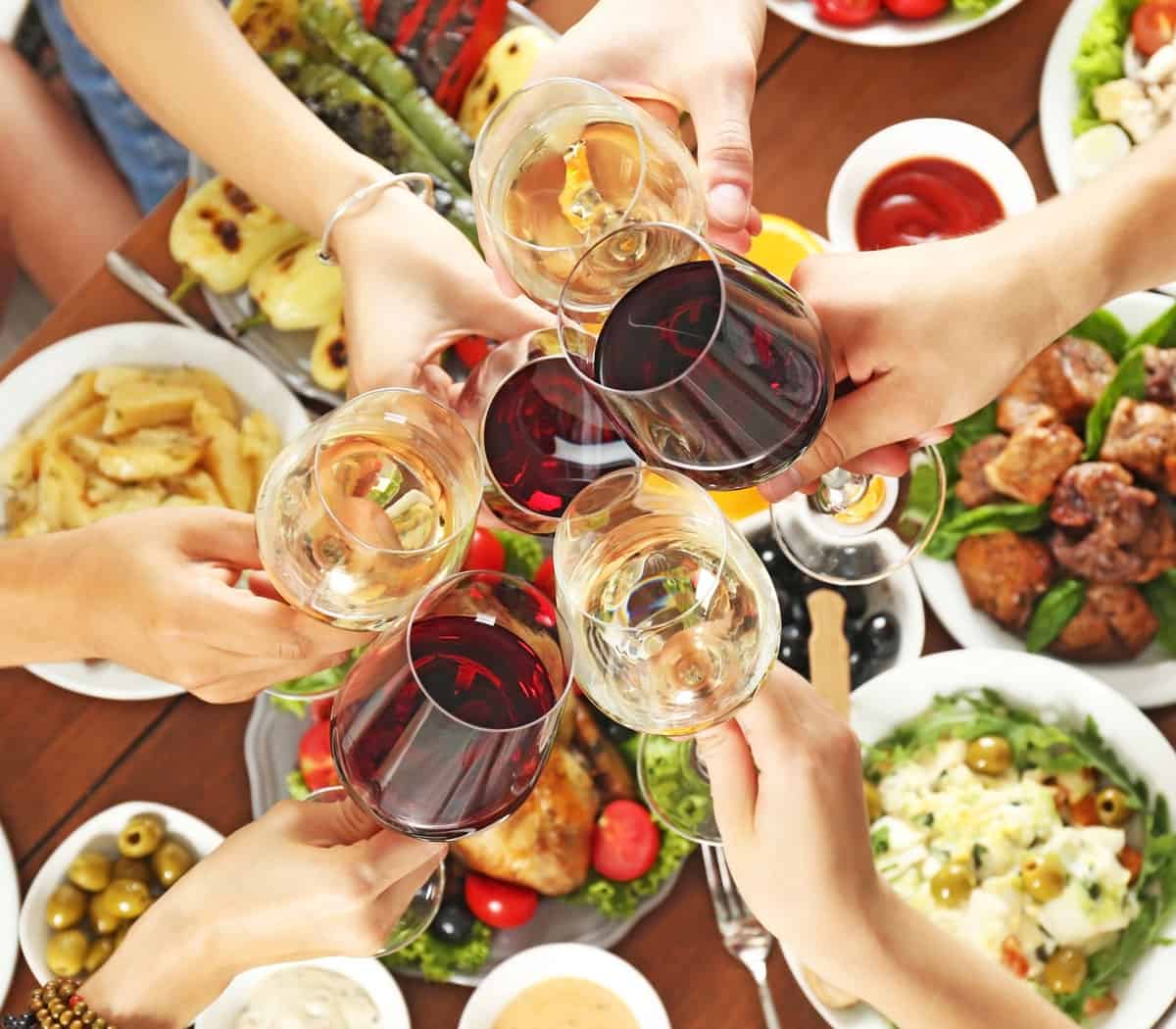 5 wine glasses toasting above a table of italian food