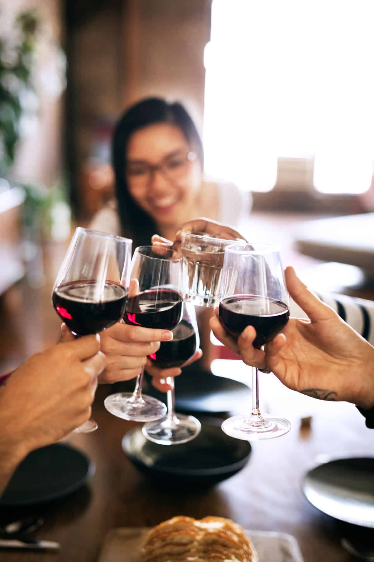 5 red wine glasses toasting with a woman in the background.