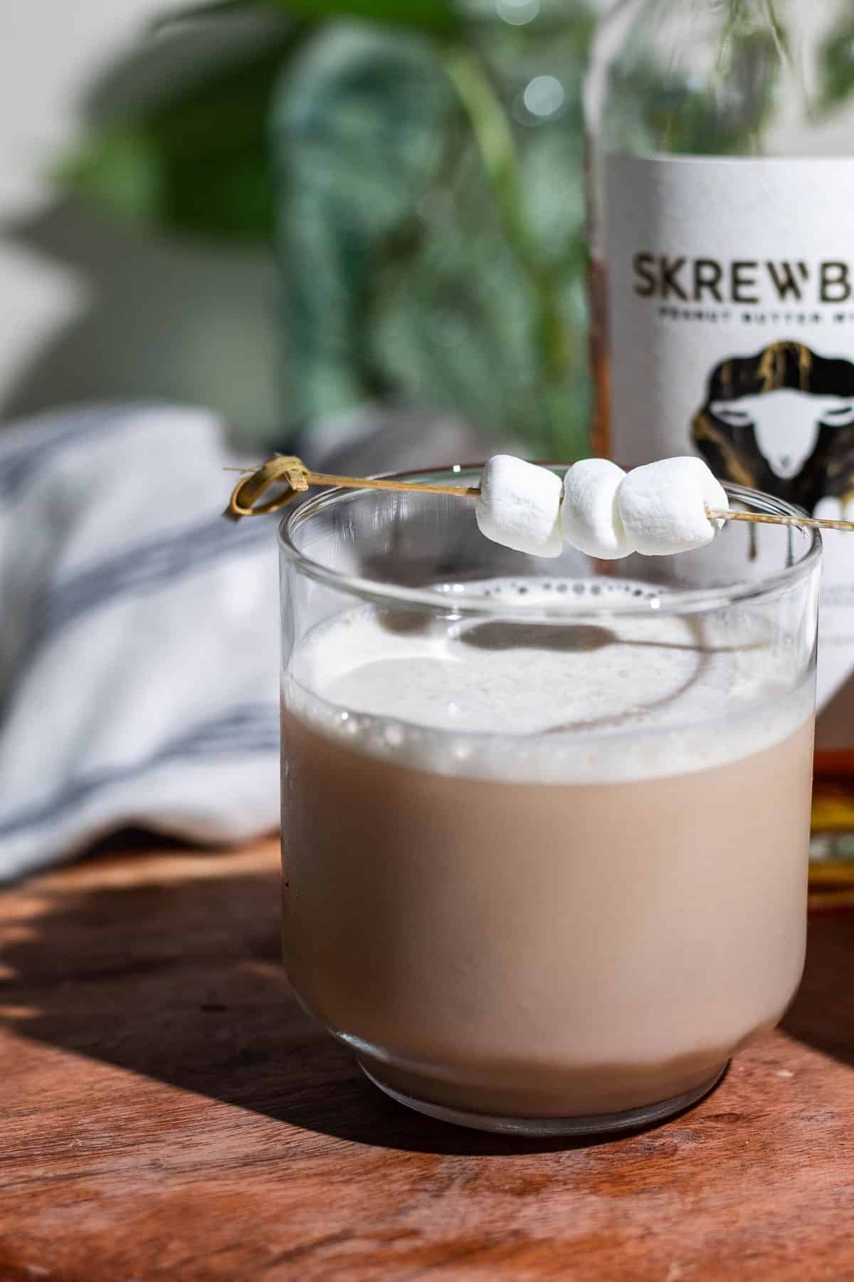 Close up of the fluffernutter cocktail garnished with marshmallows and a bottle of Skrewball peanut butter whiskey in the background.