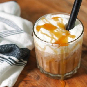 The iced latte on a cutting board with a black straw and a blue and white napkin on the side.