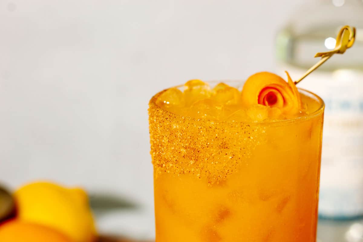 Top of the pumpkin spice margarita with a pumpkin spice sugar rim in a cocktail glass and an orange twist rolled and skewered on top.