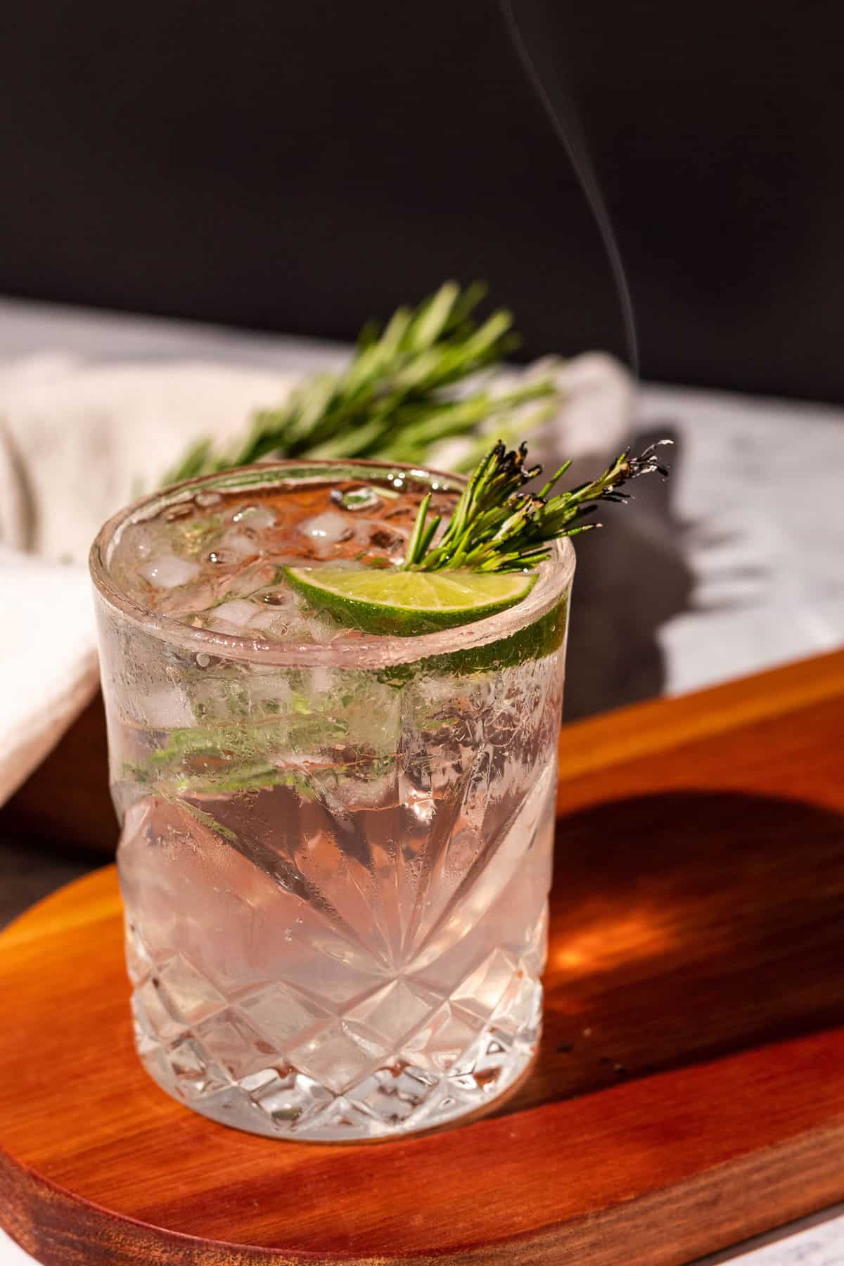 Smoked gin cocktail on a wood cutting board with a black background.