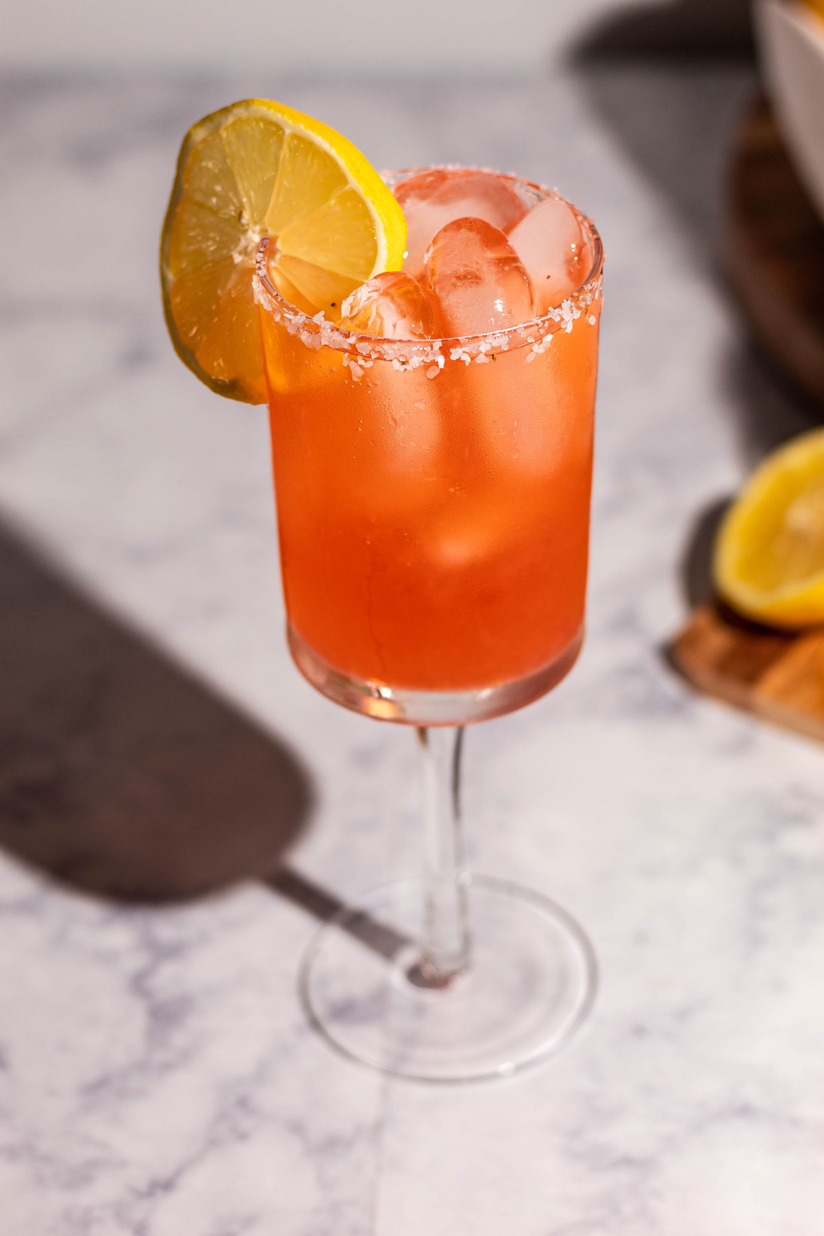 Full view of the strawberry limoncello margarita on a white marble surface with a lemon wedge garnish.