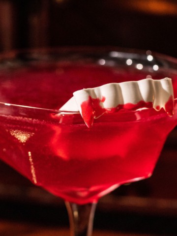 Vampire fangs with red icing draping over the rim of a martini glass.