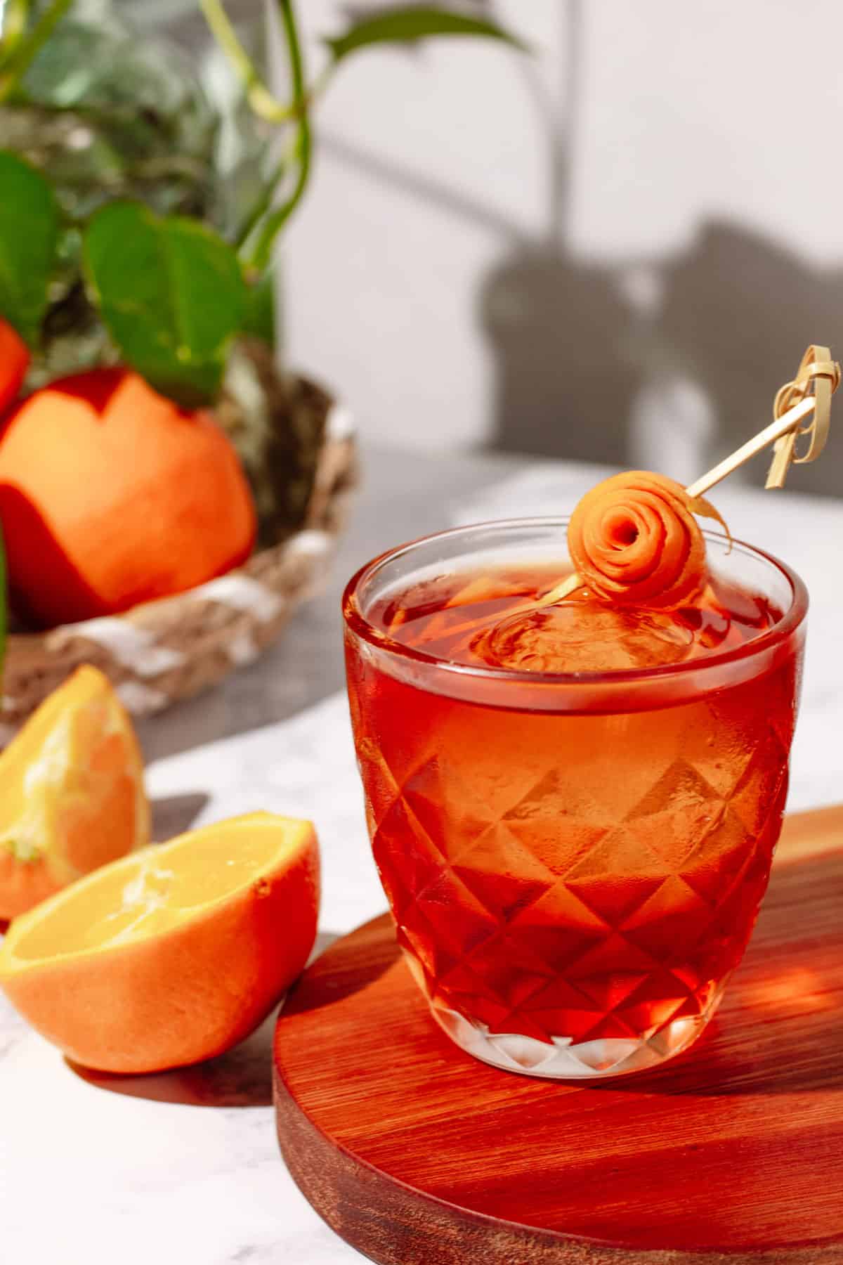 The negroni on a wood cutting board with cut and whole oranges and a green plant in the background.